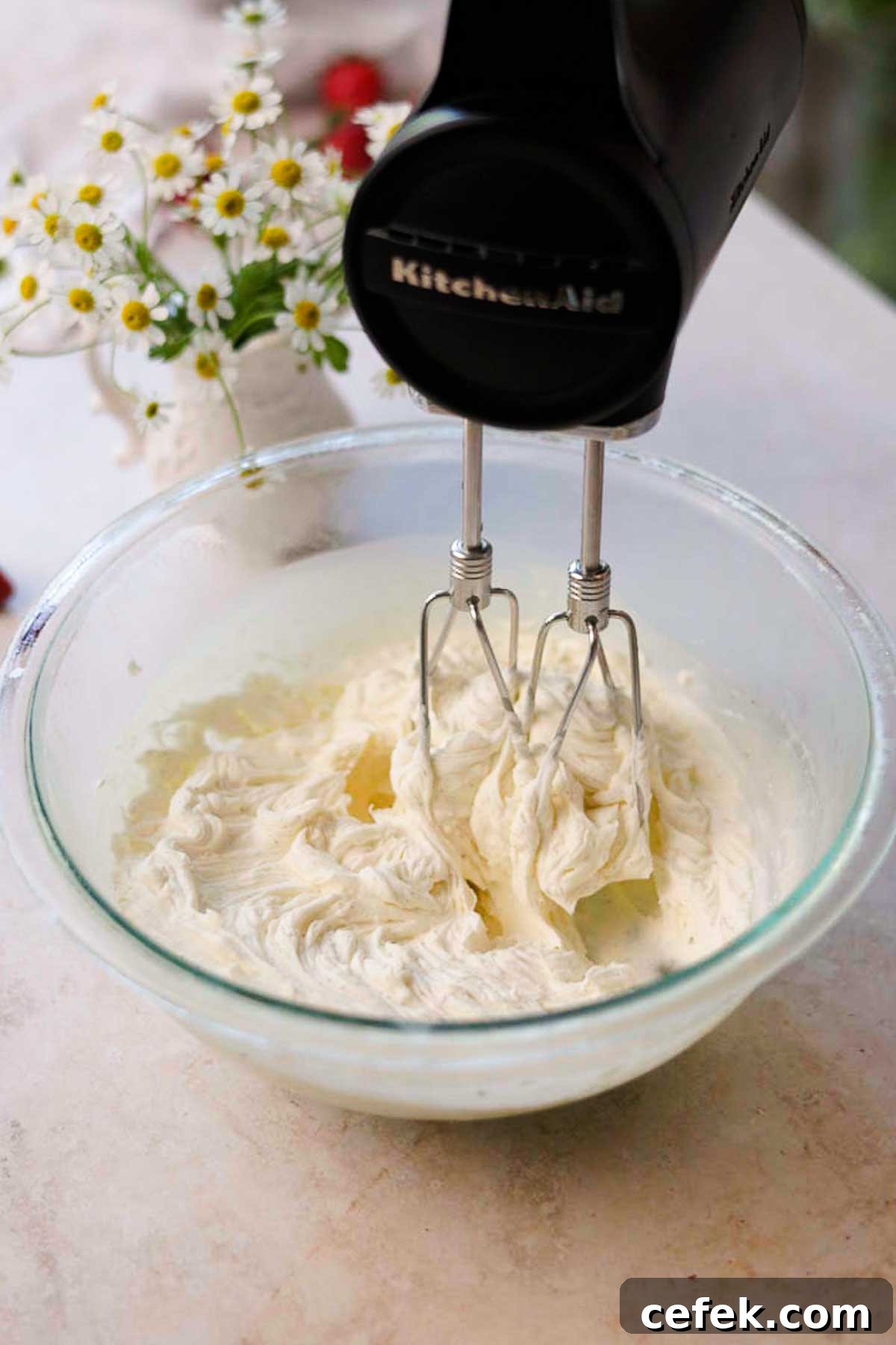 a hand held electric mixer whipping white chocolate ganache in a glass bowl