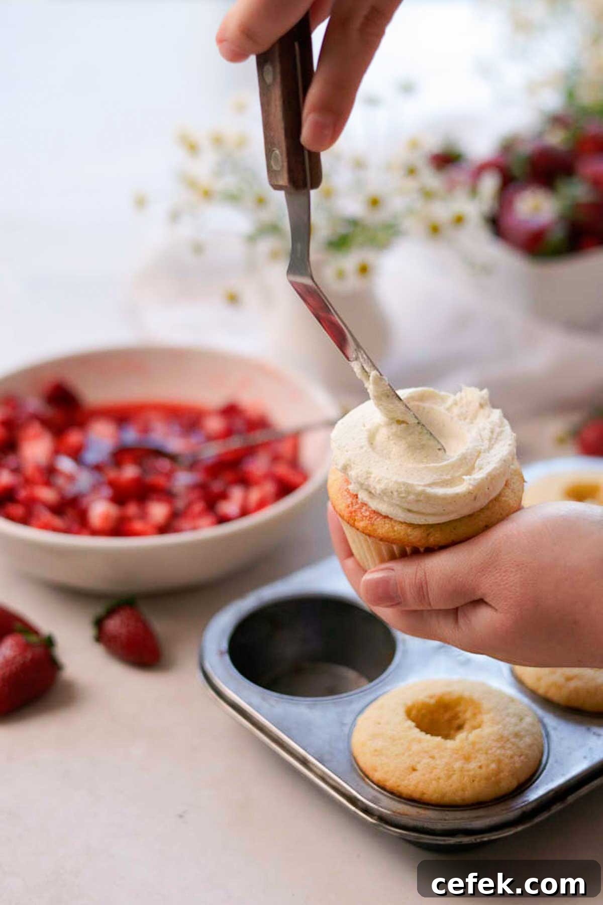 adding white chocolate mousse frosting to the cupcakes with a metal spatula