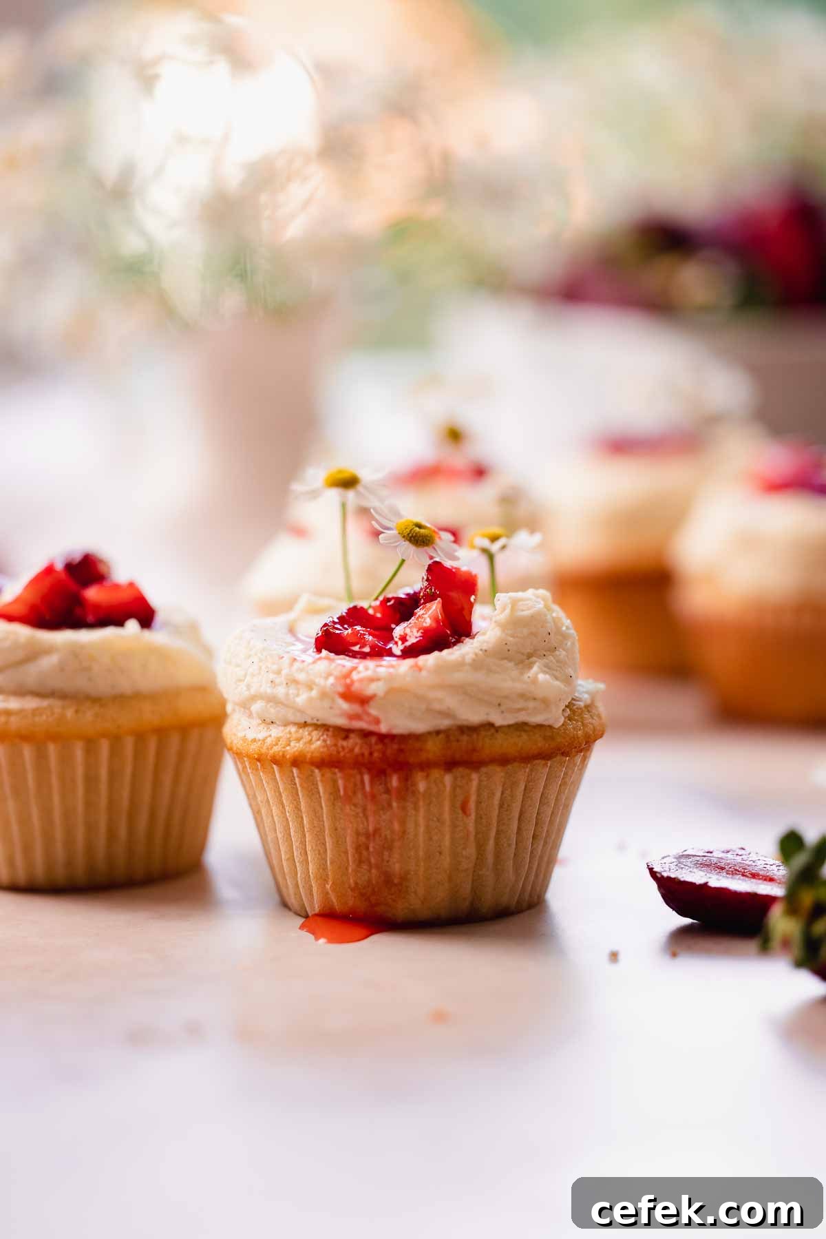 a close up of a white chocolate strawberry cupcake with some strawberry syrup dripping from the top