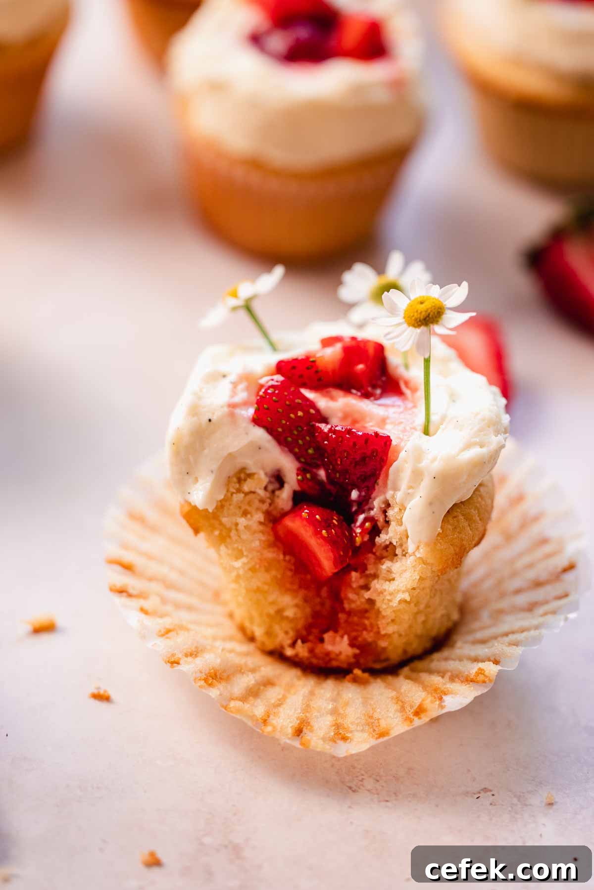 a close up shot of a bitten strawberry white chocolate cupcake with strawberries inside and flowers on top