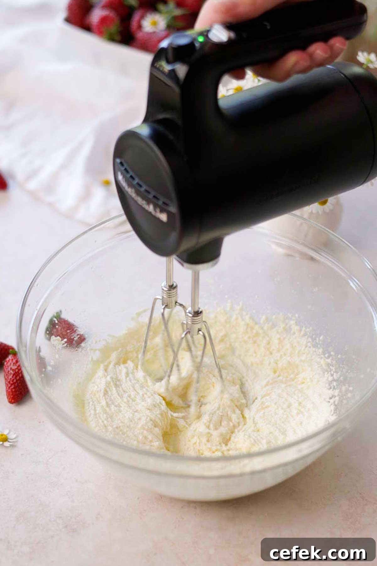 sugar, butter, and oil being whipped in a glass bowl by a hand held electric mixer