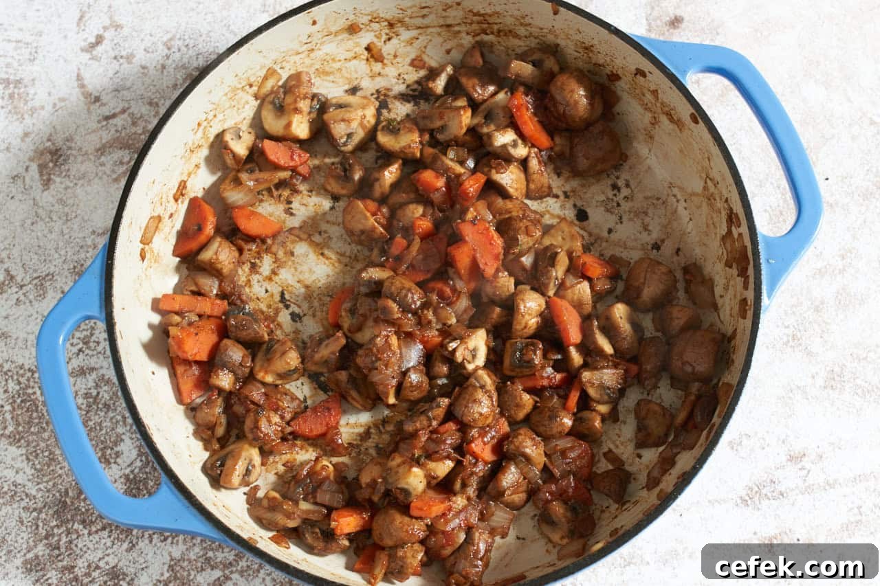 Cooked mushrooms, carrots and onions in a blue pan.