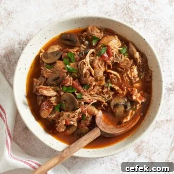 A large bowl of slow cooker chicken cacciatore with a wooden spoon in it. A red and white striped napkin is on the left.