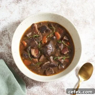 A bowl of slow cooker beef bourguignon topped with fresh thyme, a gold spoon is on the right.