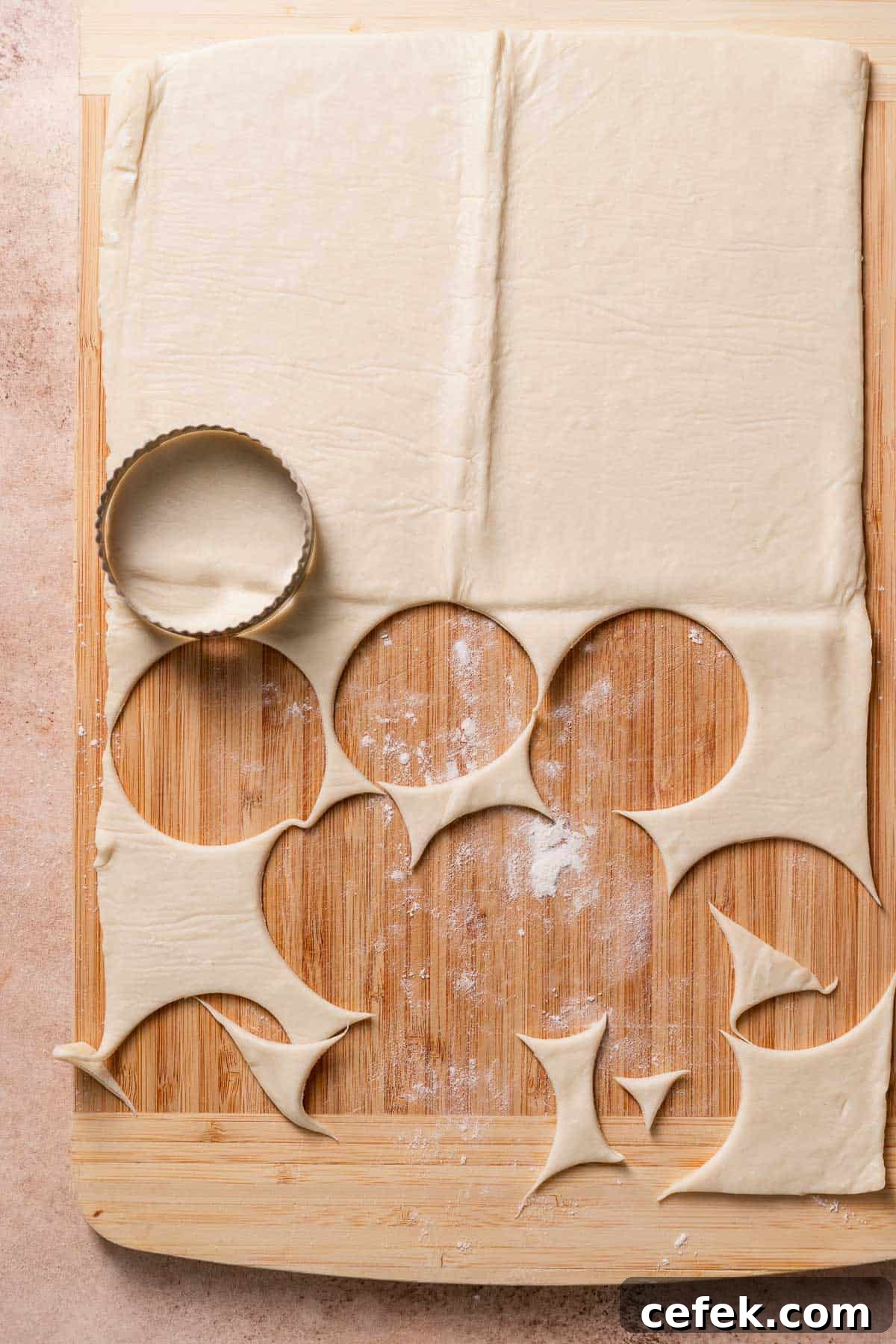 Puff pastry dough on a wooden cutting board with a round cookie cutter cutting the dough.