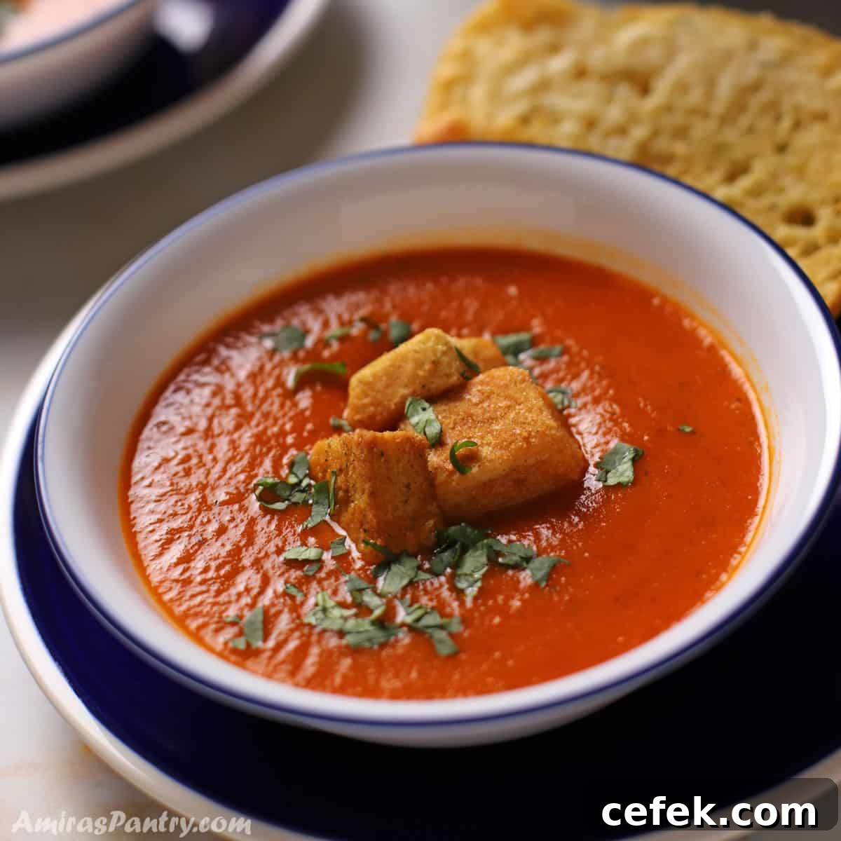 A bowl of tomato basil soup with some croutons on the top.