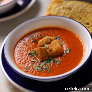 A bowl of tomato basil soup with some croutons on the top.