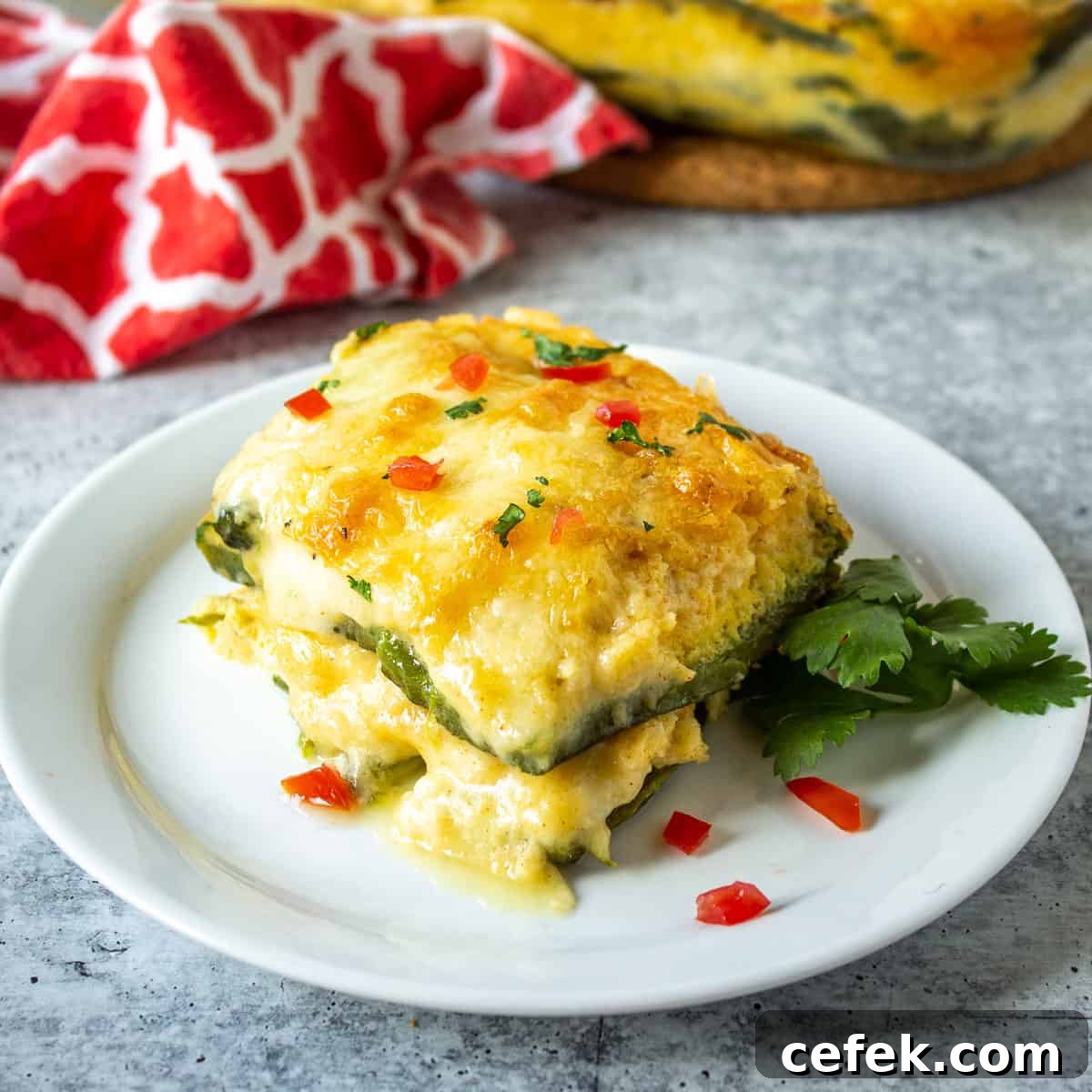 A slice of chili relleno casserole topped with finely diced tomatoes and fresh cilantro.