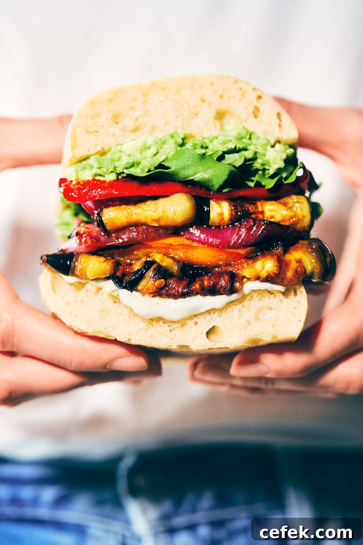Roasted veggie sandwich with roasted zucchini and peppers, avocado and mayo being held in front of a white shirt