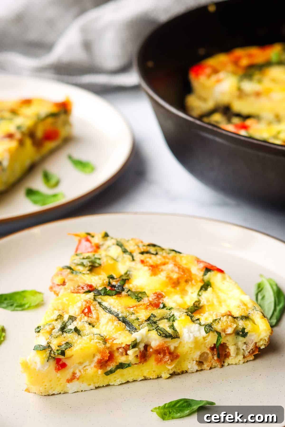 a slice of goat cheese frittata on a plate with fresh basil leaves on the side