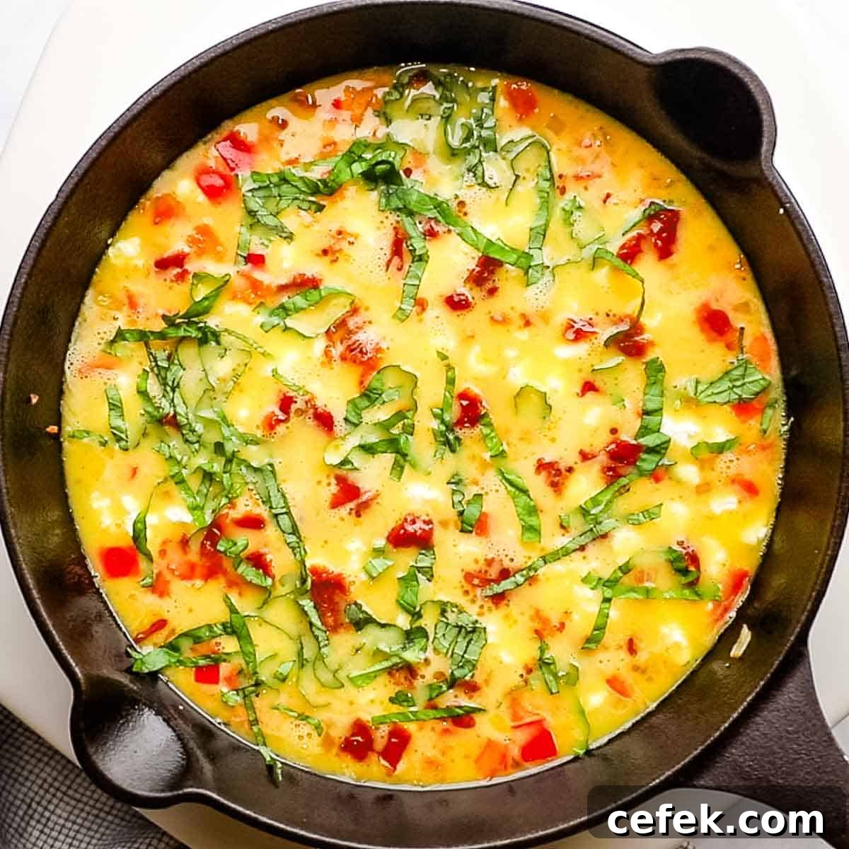 basil, sundried tomato, and goat cheese added to the egg mixture in the skillet