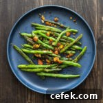 A single portion of seared green beans with toasted spiced almonds sitting on a blueish gray round plate with a rustic brown table.