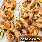 Close up image of grilled shrimp on wooden skewers. On a light colored speckled plate topped with chopped parsley.