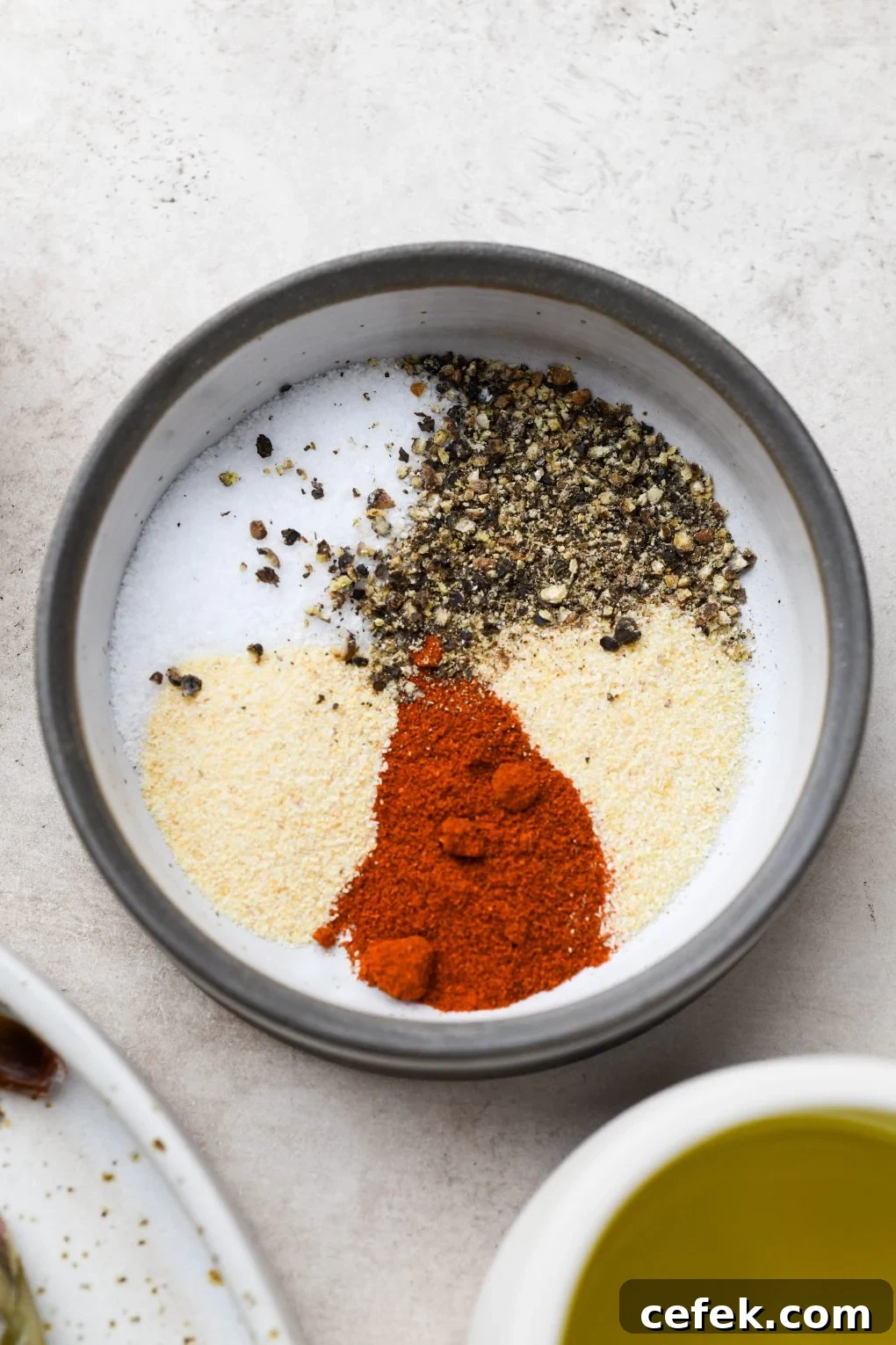 Small shallow bowl filled with a spice blend of paprika, garlic powder, onion powder, salt, and pepper. On a light colored background.