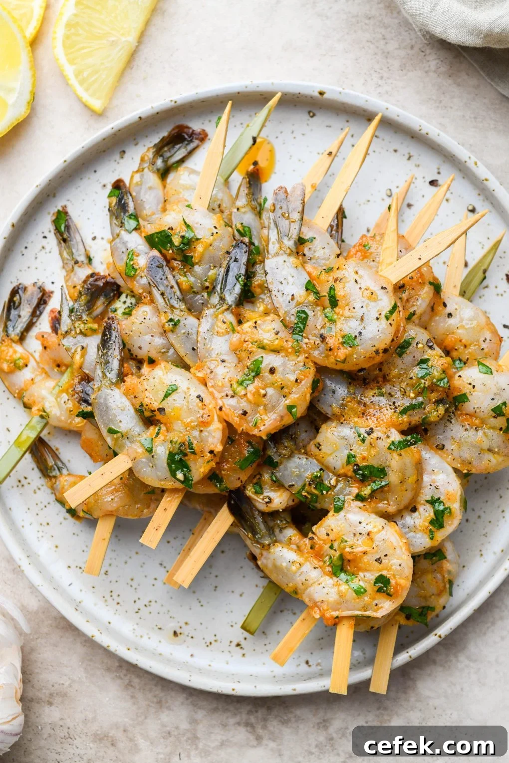 Overhead image of marinated shrimp threaded onto short wooden bamboo skewers. On a light colored speckled plate.