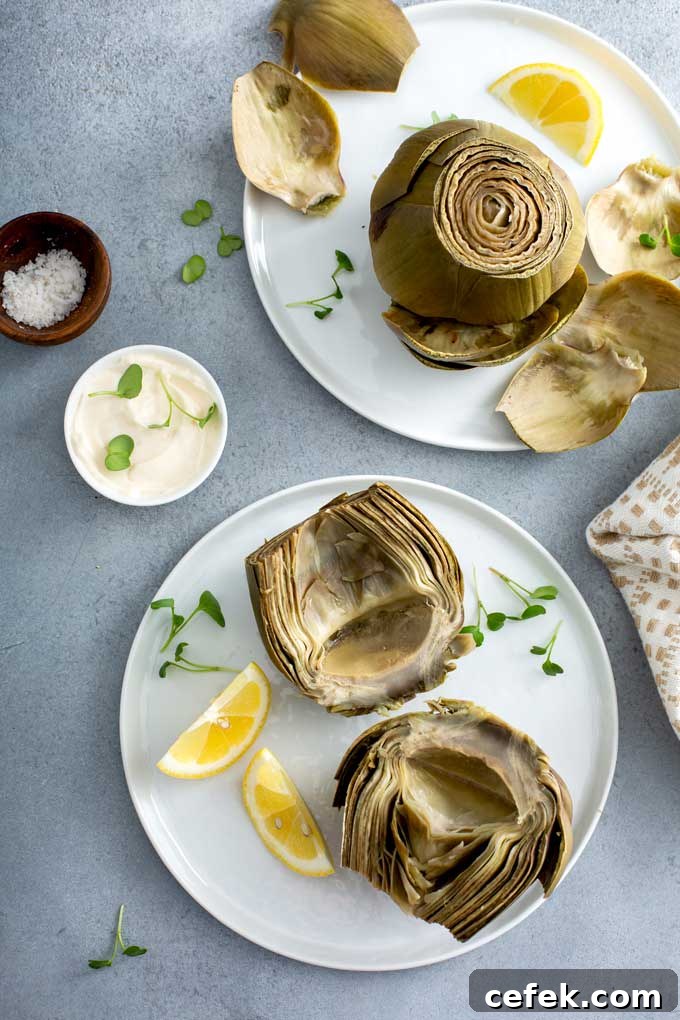 Artichokes on white plates served with lemon slices and dipping sauce
