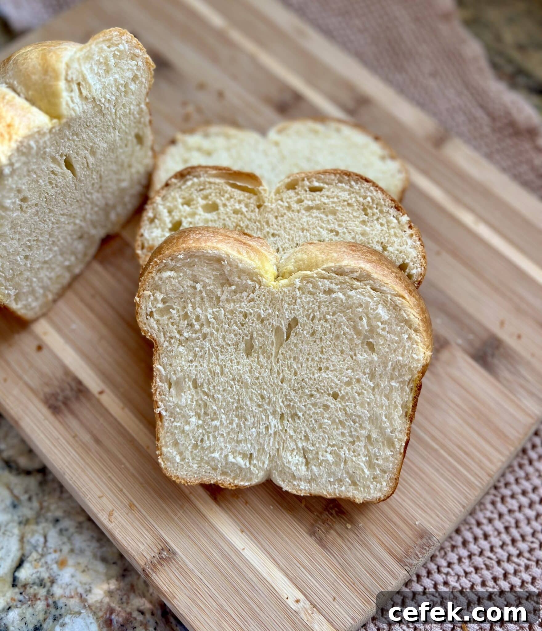 Three slices of sourdough brioche bread sit on a cutting board next to the rest of the loaf.