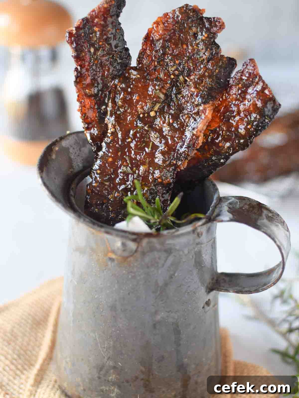 Candied bacon with rosemary and fig in a metal serving pitcher.