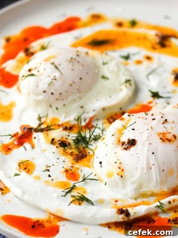 Two eggs on a white dish with chili butter on top with fresh dill.