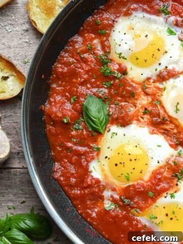 Overview of poached eggs in a skillet with tomato sauce with bread.
