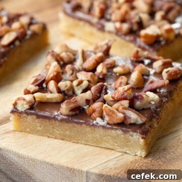 toffee squares topped with nuts on a wooden board.