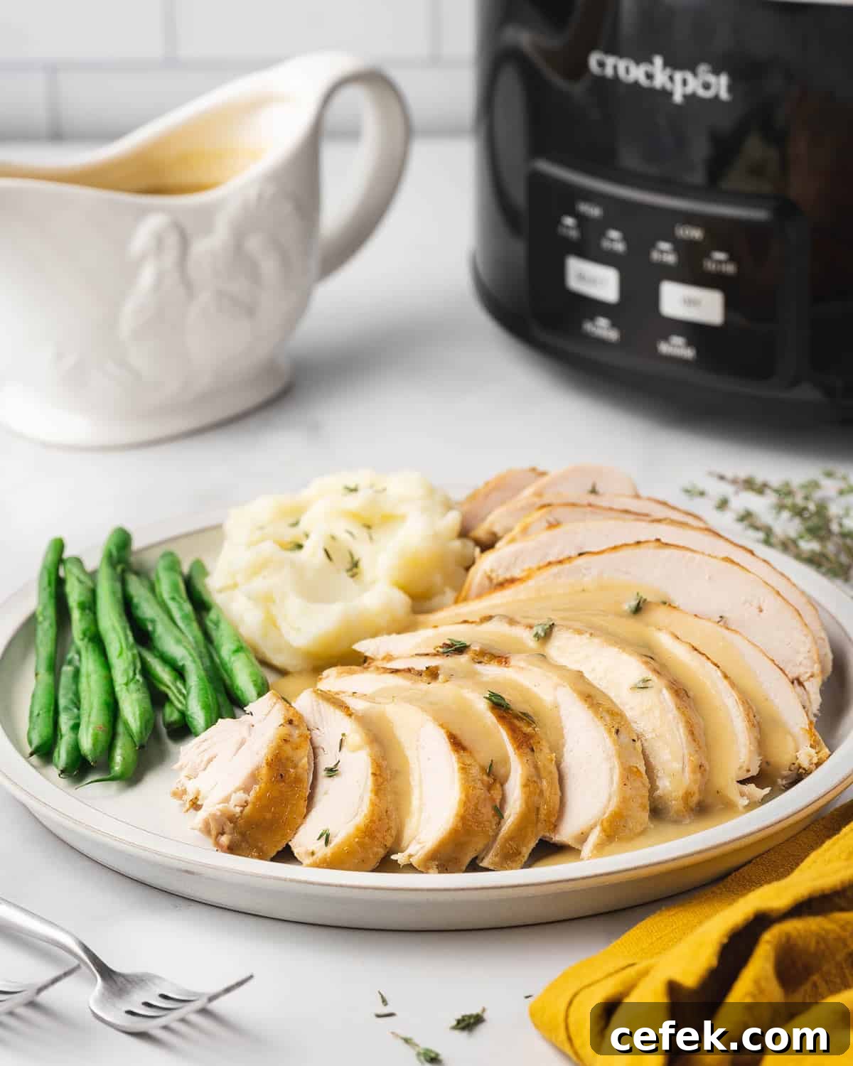 A plate of sliced turkey breast with green beans and mashed potatoes with a slow cooker in the background.