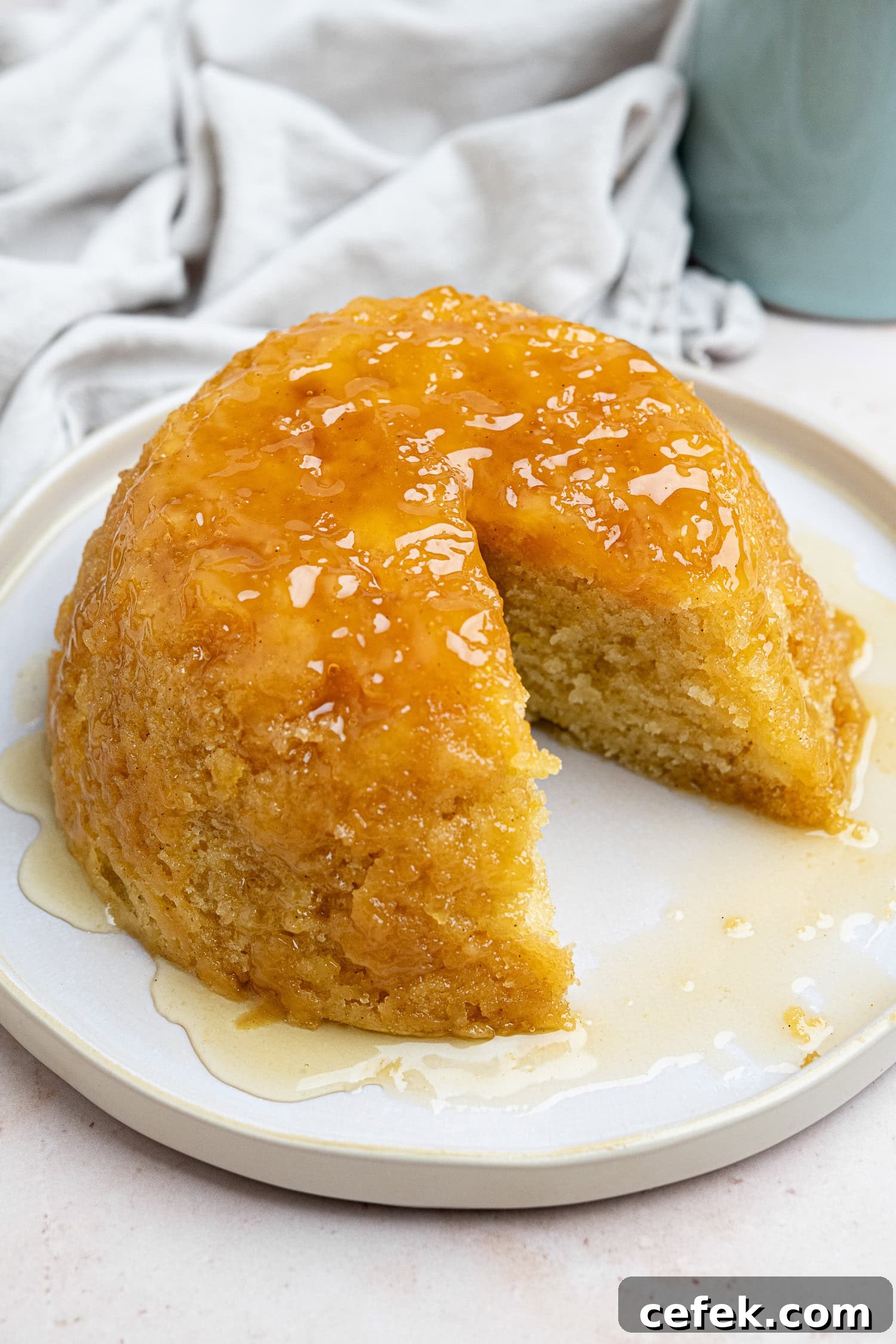 Steamed syrup sponge pudding on a white plate with a slice removed.