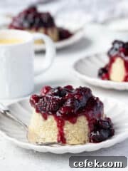 Three steamed berry and coconut puddings on plates with a jug of custard.