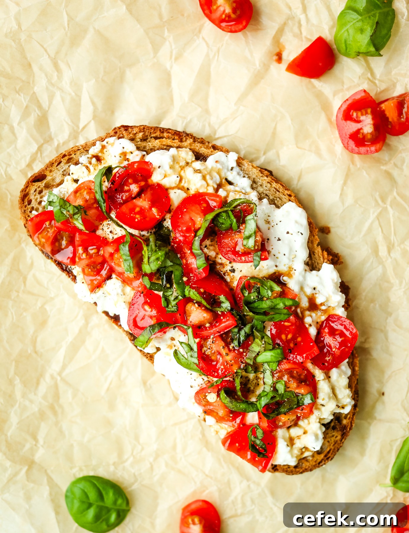 A slice of toast with cottage cheese, quartered grape tomatoes,and strips of basil