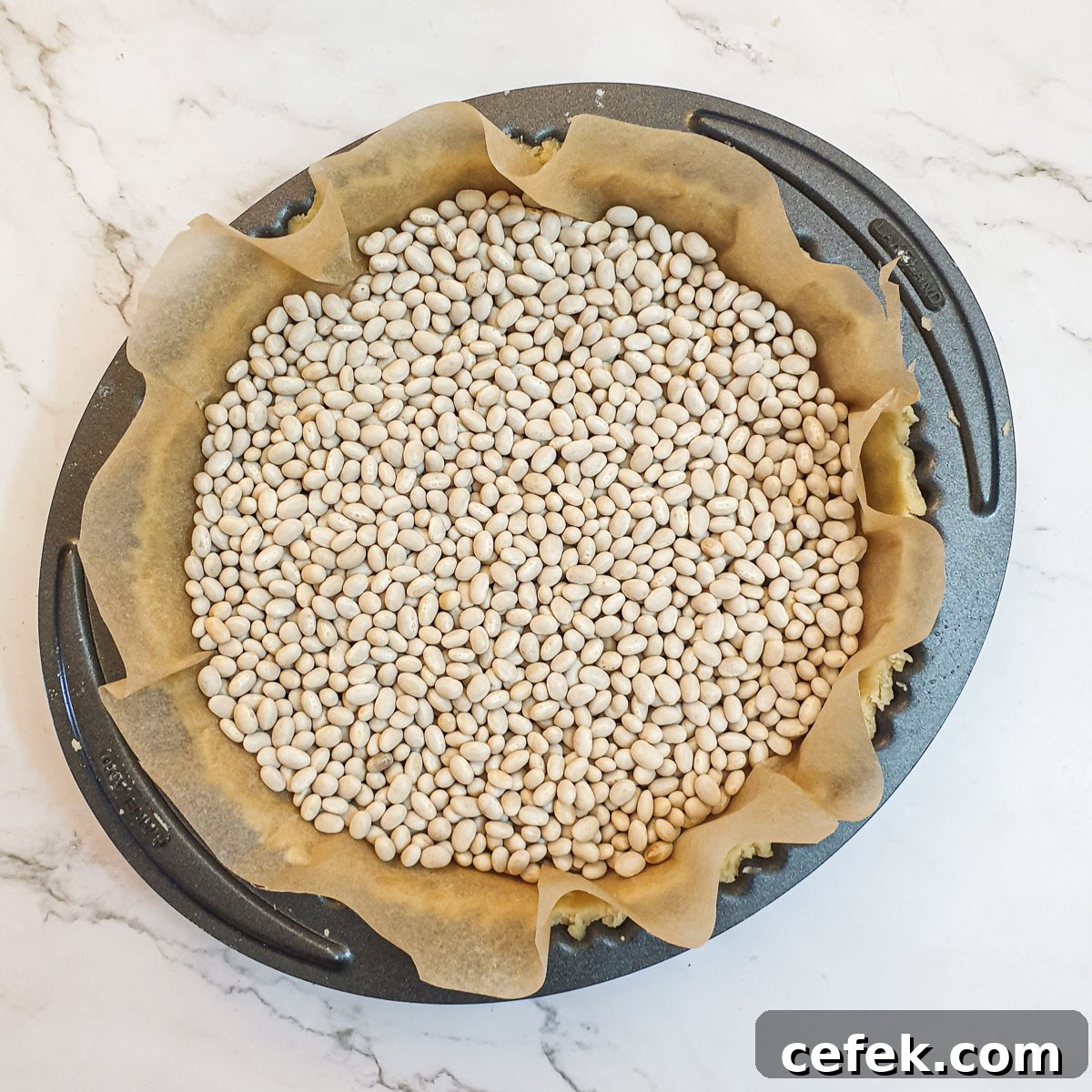 A pastry case lined with baking parchment and filled with dry beans.