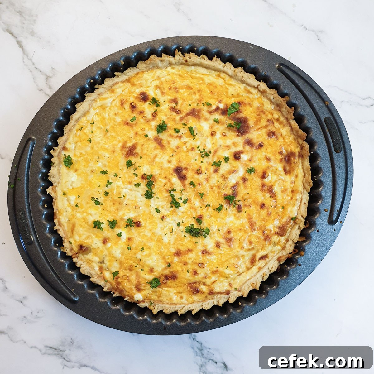 A baked cheese and onion quiche sprinkled with chopped parsley.