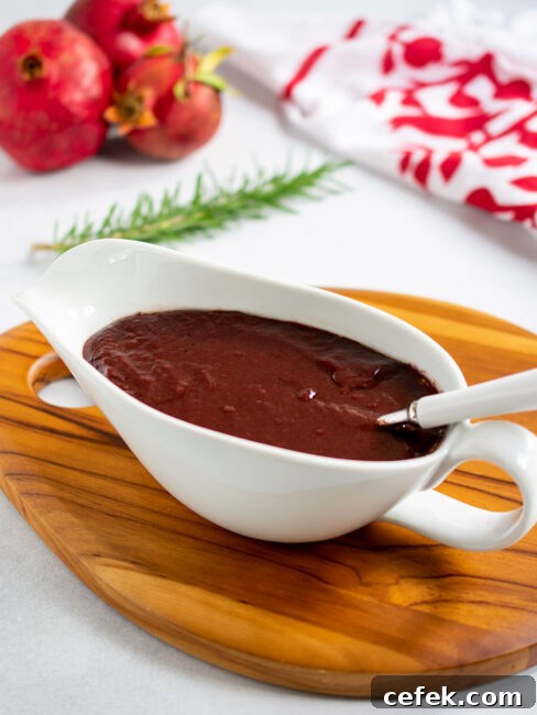 Pomegranate gravy in a white gravy boat with a white handled spoon with pomegranates in the background.