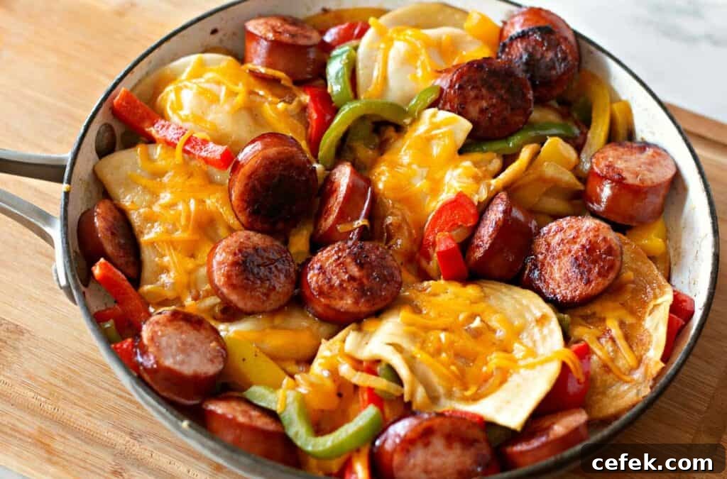 A skillet filled with kielbasa, sliced sausages, red and green bell peppers, onions, and melted cheese on top of sliced potatoes creates a delicious harmony reminiscent of a classic pierogi meal.