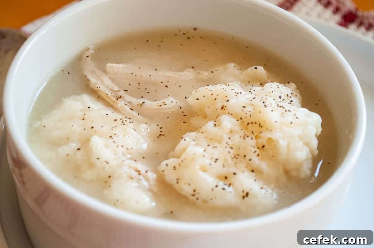 Soft dumplings in a white bowl with chicken and black pepper.