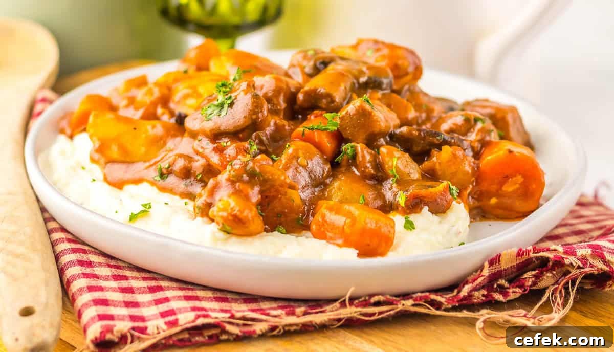 Slow cooker beef bourguignon with carrots and mushrooms served over mashed potatoes.
