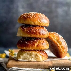 A stack of four gluten free burger buns with one leaning to the side, next to small yellow flowers on a wooden board.