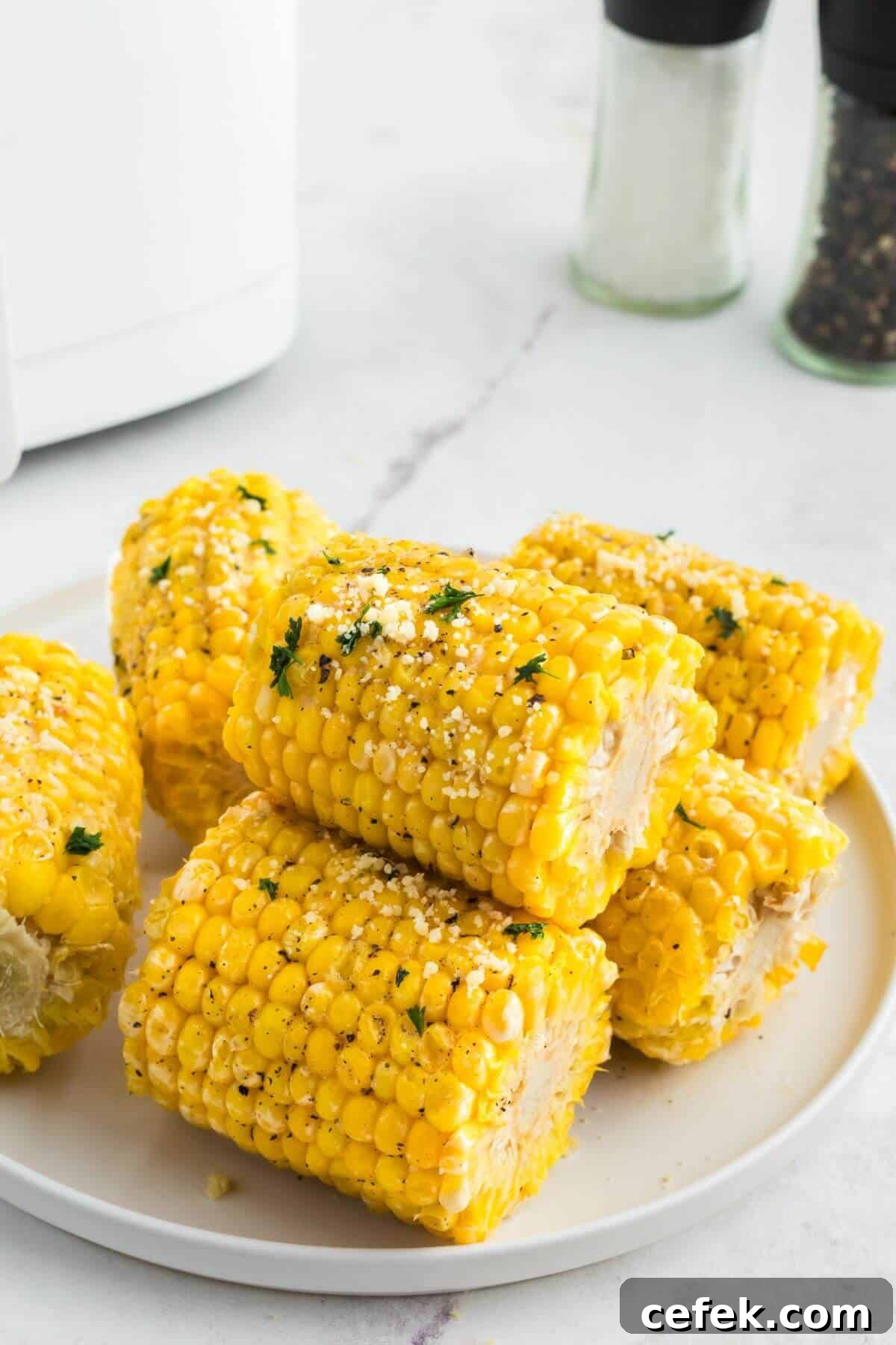 Golden yellow ears of corn stacked on a white plate garnished with parsley flakes. 