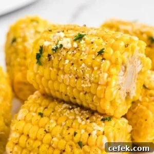 Golden yellow ears of corn stacked and garnished with parmesan cheese and parsley flakes.