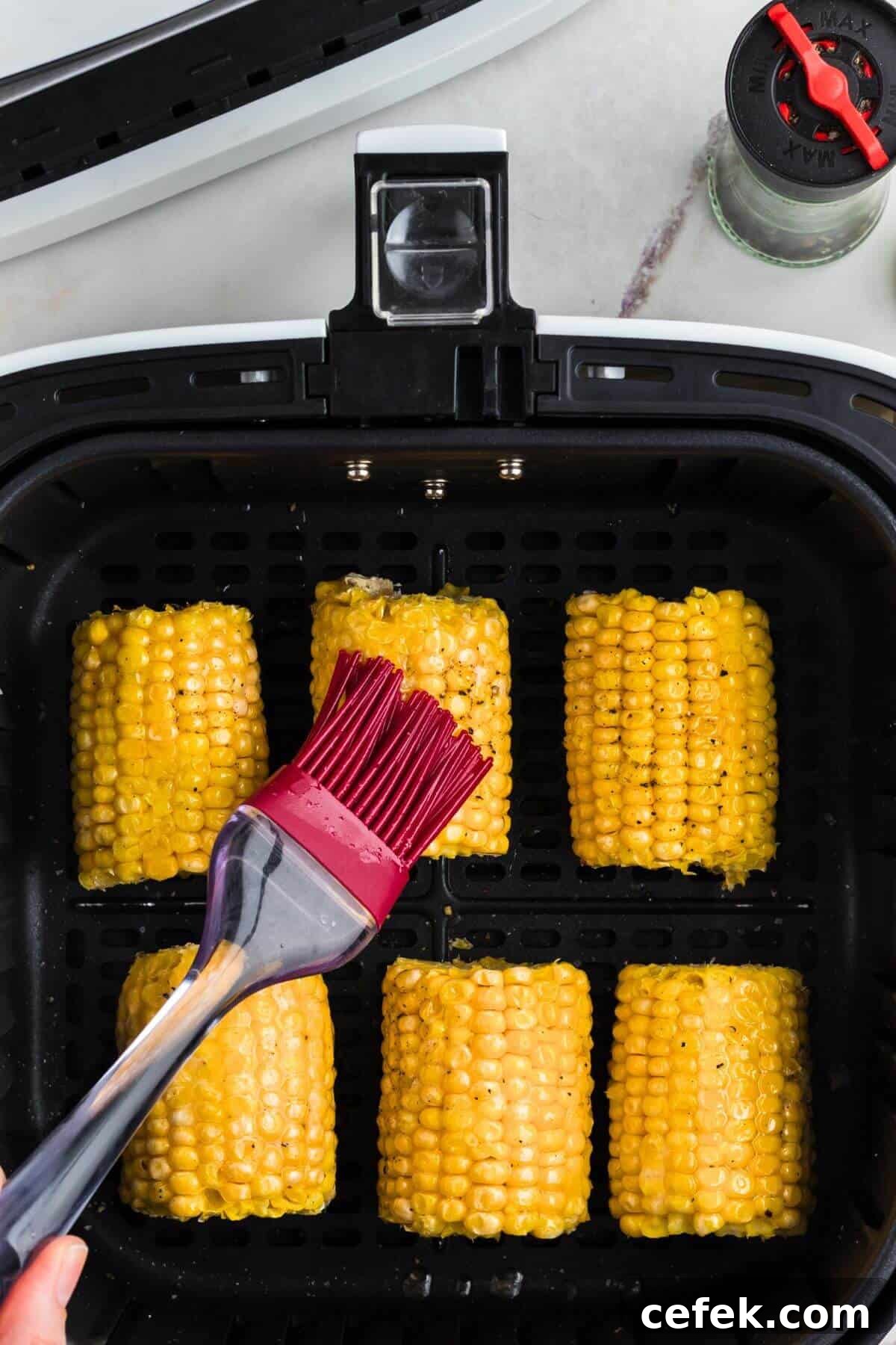 Brushing melted butter on corn along with salt and pepper. 