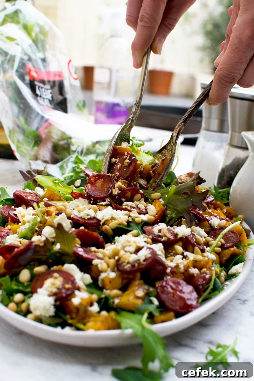 A person serving an Amazing Roast Pumpkin, Chorizo And Feta Salad with salad servers