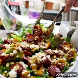 A person serving warm butternut squash, chorizo and feta salad with salad servers