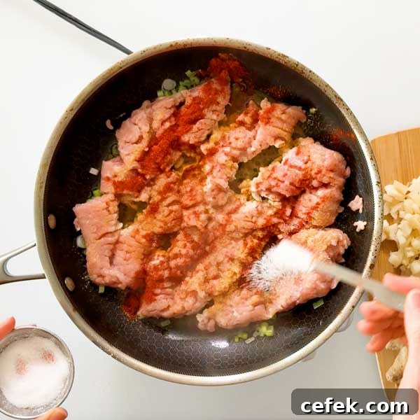 Sprinkling the dry seasonings over the meat in the skillet.