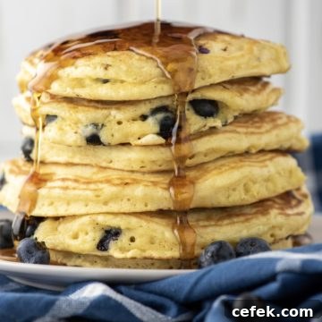 maple syrup being drizzled over stacked blueberry pancakes