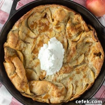 Apple Dutch baby with whipped cream in cast iron skillet.