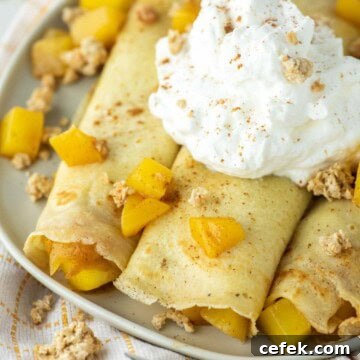 3 mango crepes rolled up on plate with whipped cream on top.