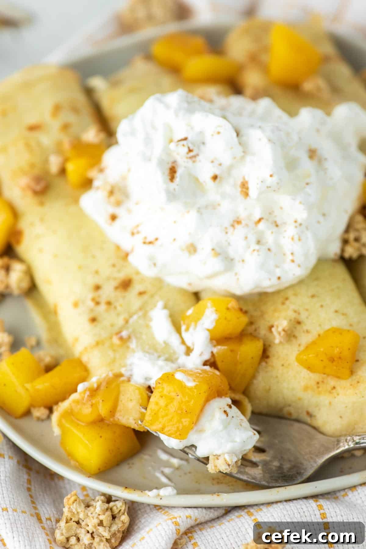 Fork taking bite of crepes with mango inside.