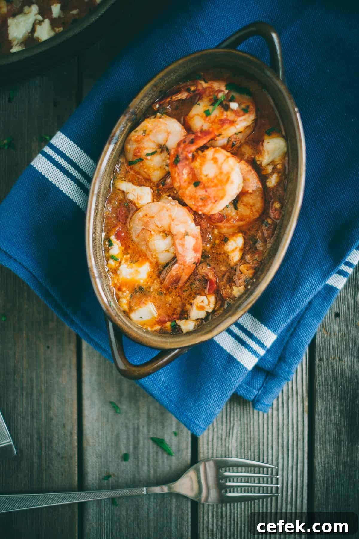 Prawn saganaki served in a claypot dish with ouzo on a wooden table
