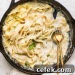 A cast iron skillet with noodles and homemade alfredo sauce and a spoon and fork sticking out.