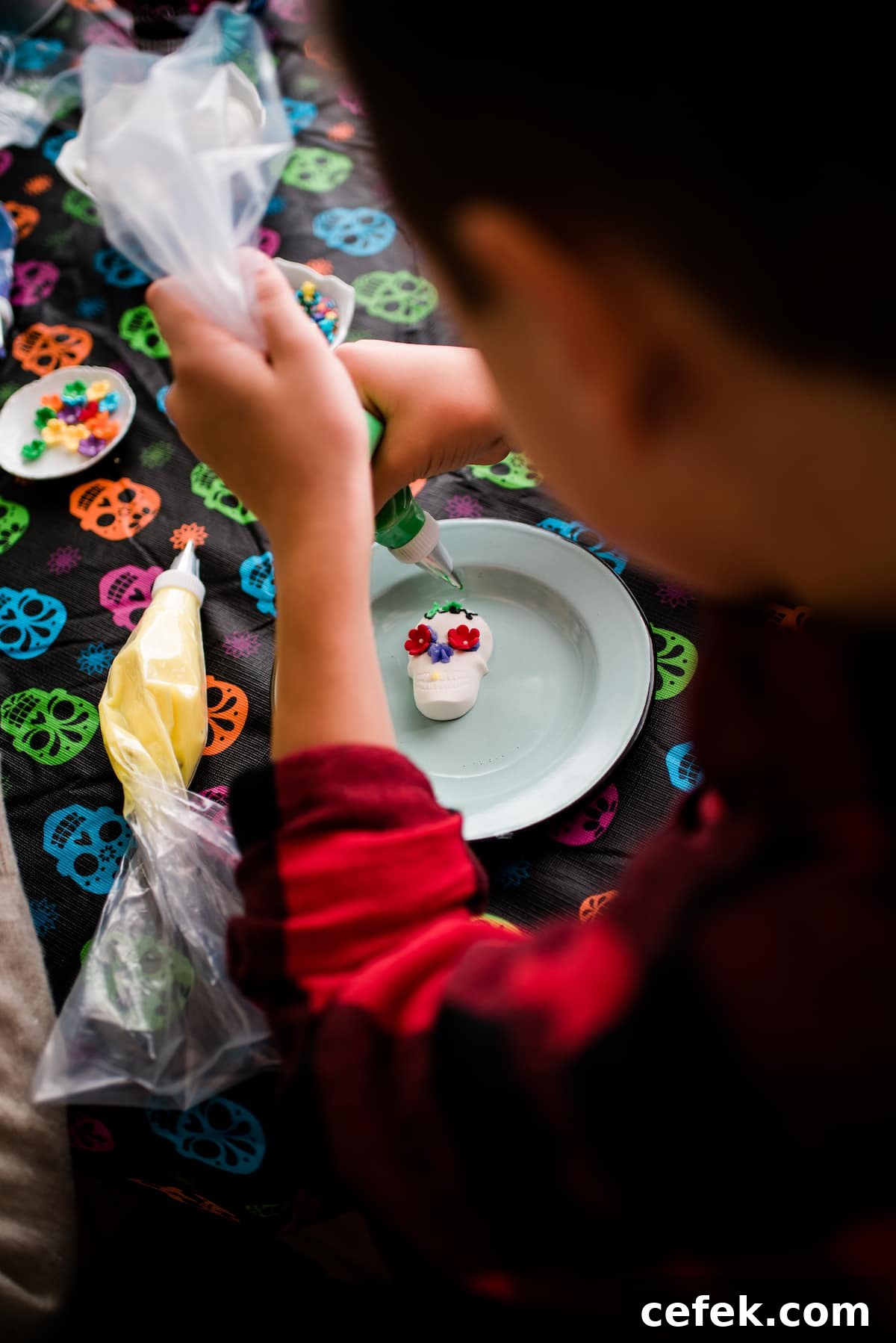 A young child decorating a Dia de los Muertos candy skull with colorful frosting, candy flowers, and sprinkles