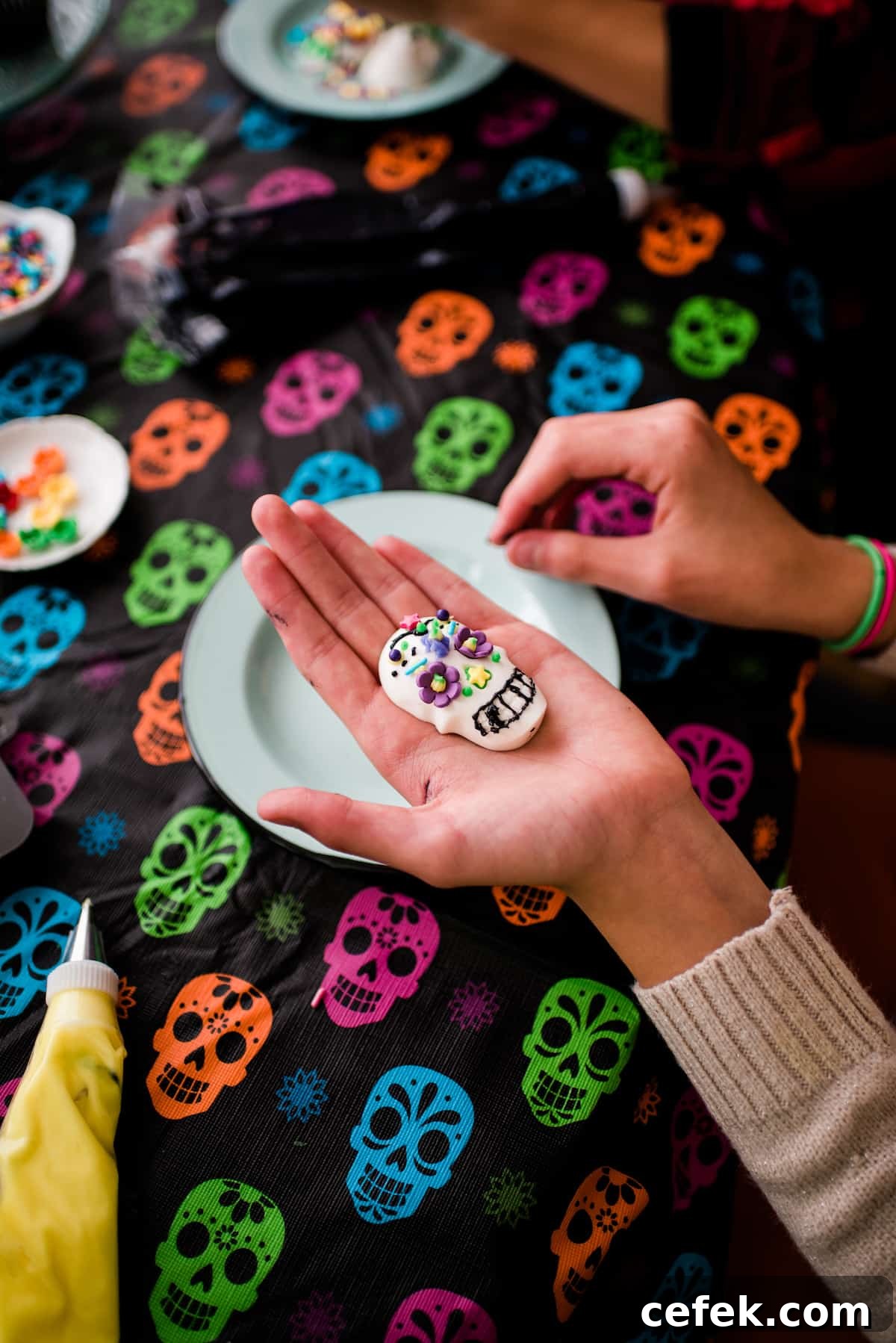 Children decorating candy skulls with frosting and sprinkles on a skull tablecloth